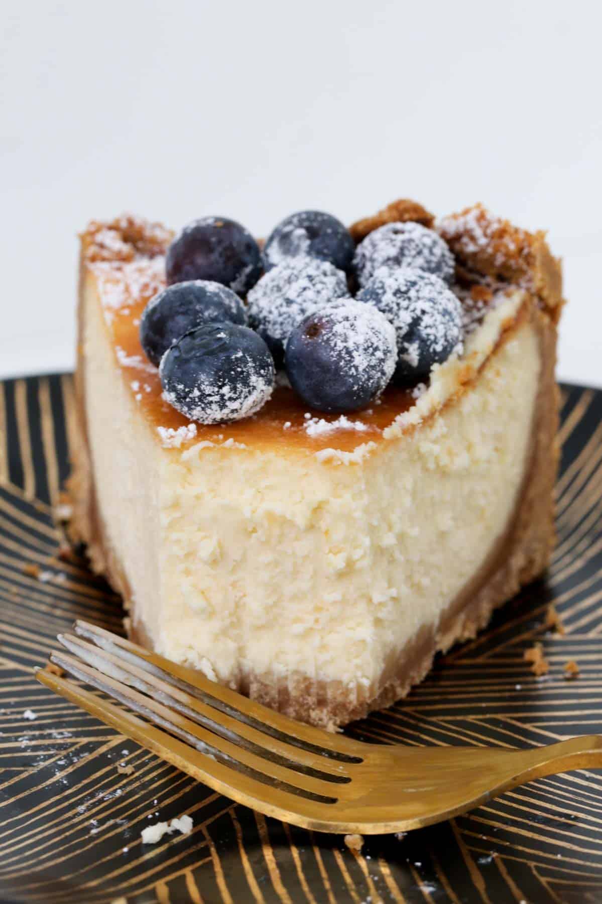 A half eaten piece of New York cheesecake with blueberries on top.