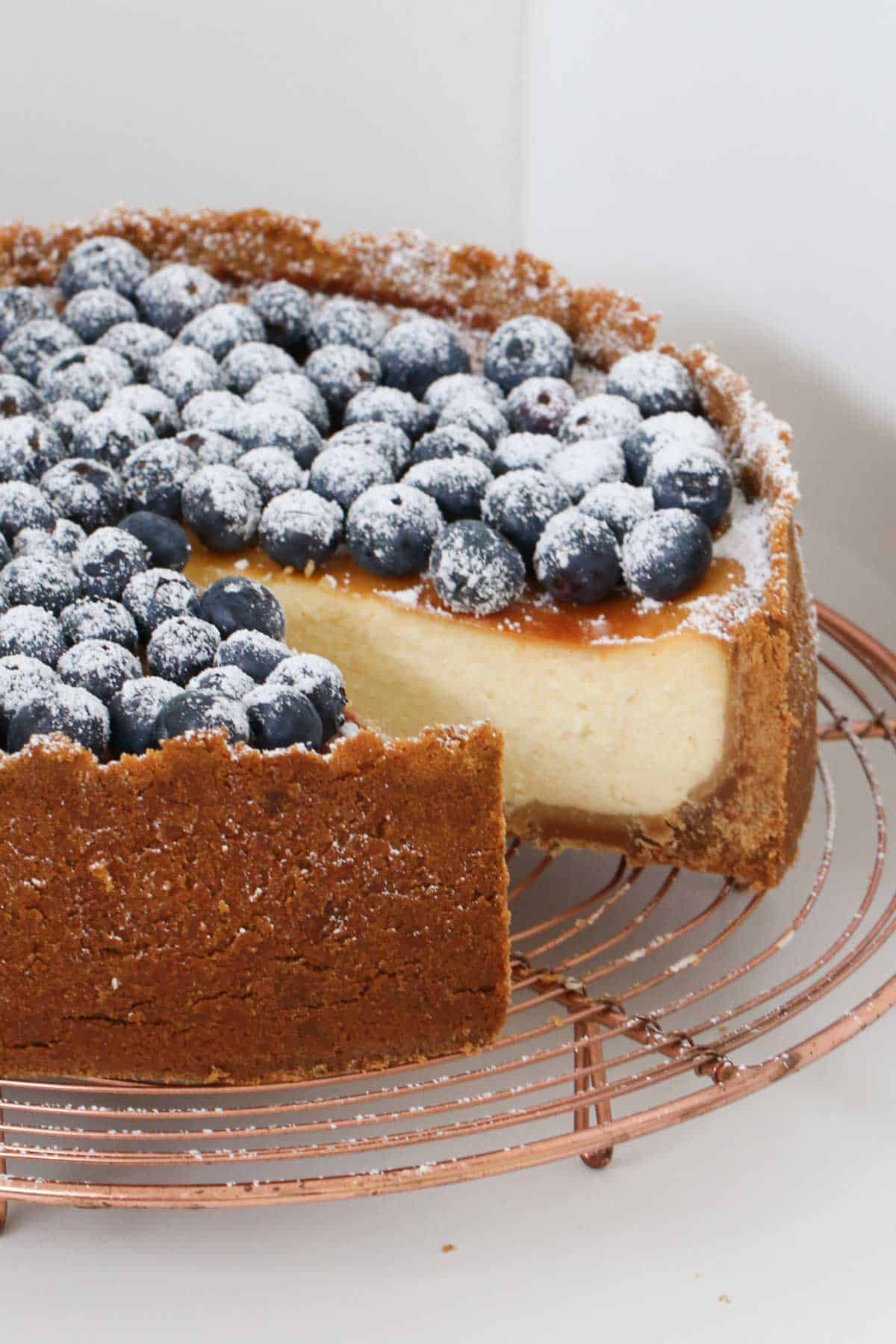A cheesecake topped with blueberries on a copper tray, with one slice removed.