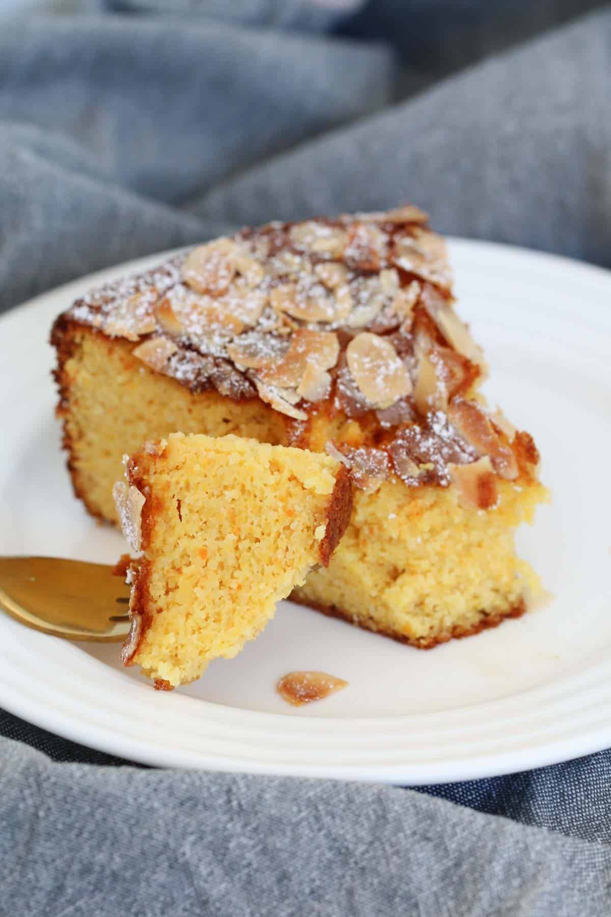 A forkful of almond and orange cake from a serve of cake on a plate.
