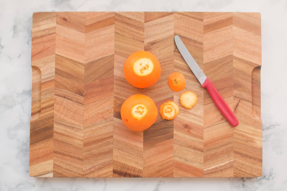 Two oranges on a chopping board and a knife.