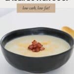A black rustic bowl filled with creamy soup and crispy bacon pieces sprinkled over.