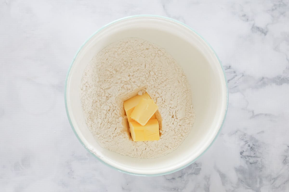 Pieces of butter added to dry ingredients in a bowl.