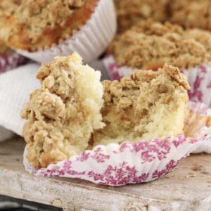 A apple streusel topped muffin in a pink and white paper case.