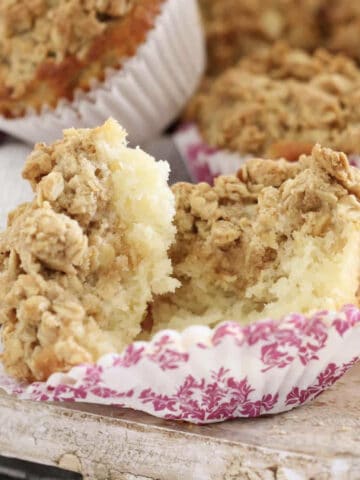 A apple streusel topped muffin in a pink and white paper case.