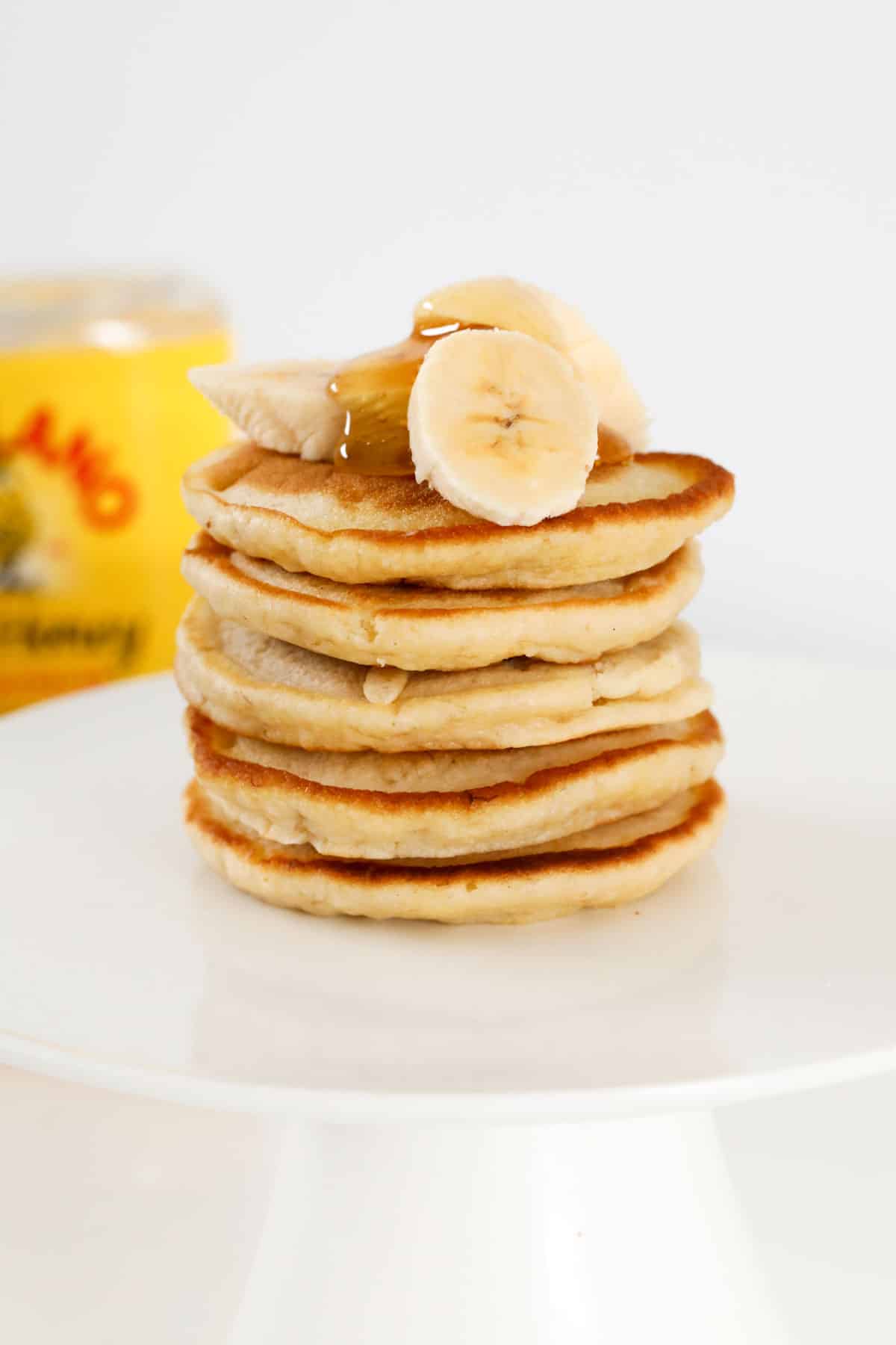 A stack of banana pikelets with banana and honey on top.