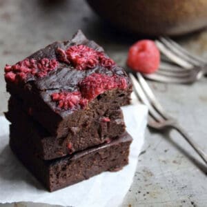 3 pieces of chocolate brownie with raspberries stacked on top of one another.