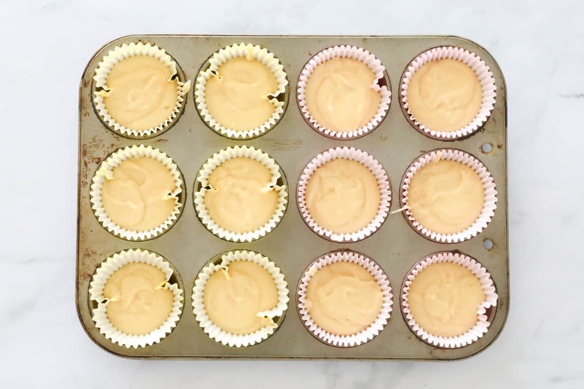 Unbaked lemon cupcakes in paper cases in a muffin tray.