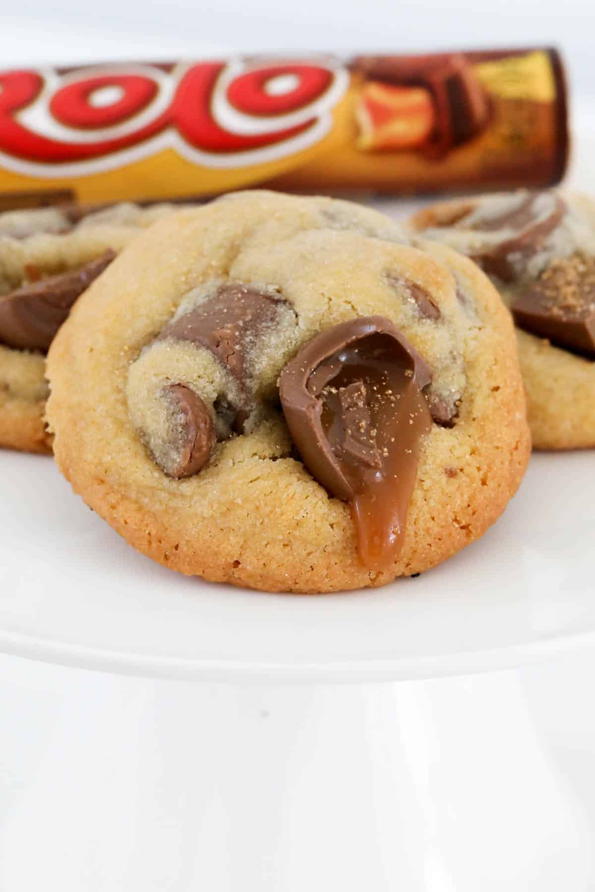 A gooey Rolo chocolate oozing out of a chocolate chip cookie.