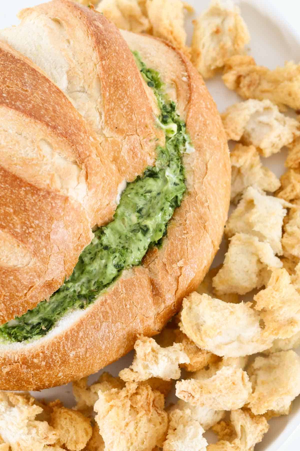 A bread loaf filled with dip and surrounded by small pieces of bread.