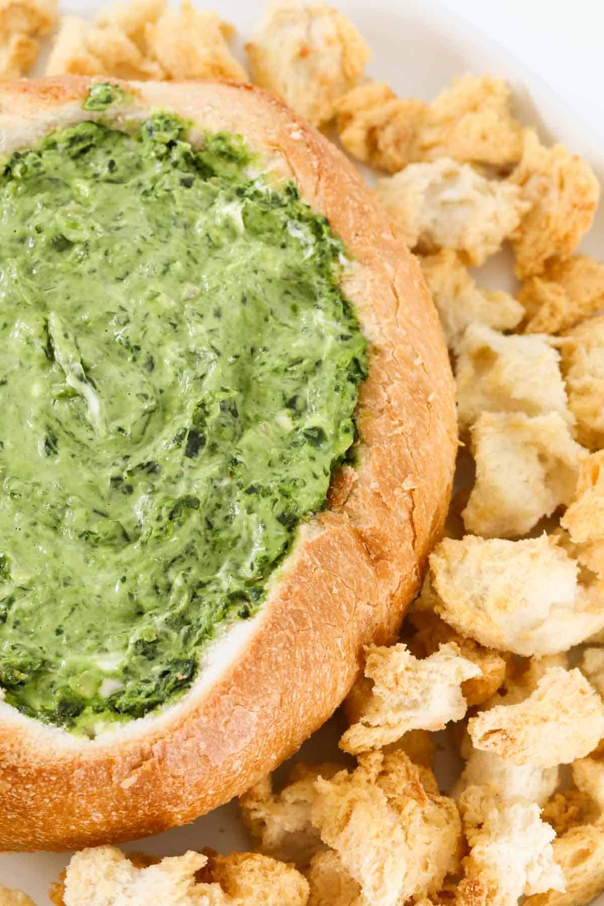 Green creamy dip inside a round bread loaf surrounded by pieces of bread.