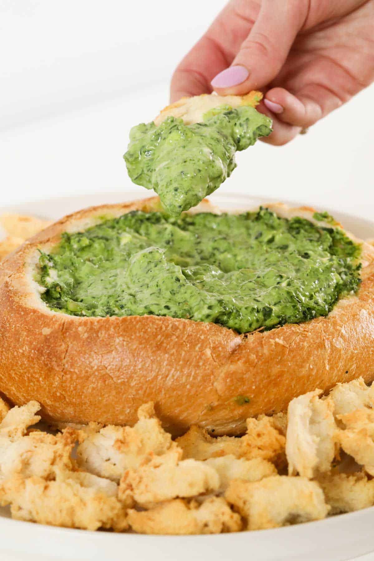 A hand dipping bread into spinach cob loaf dip.