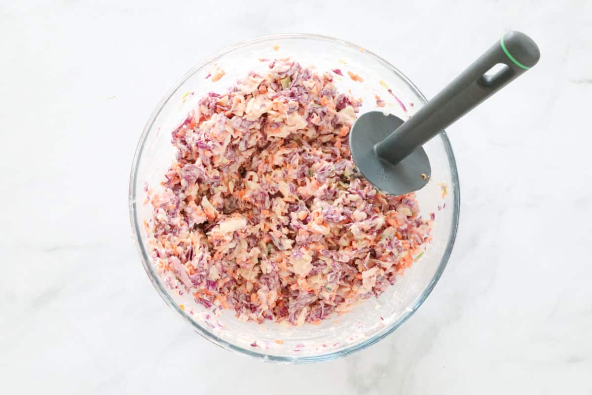 Mixed coleslaw in a bowl with a spatula.