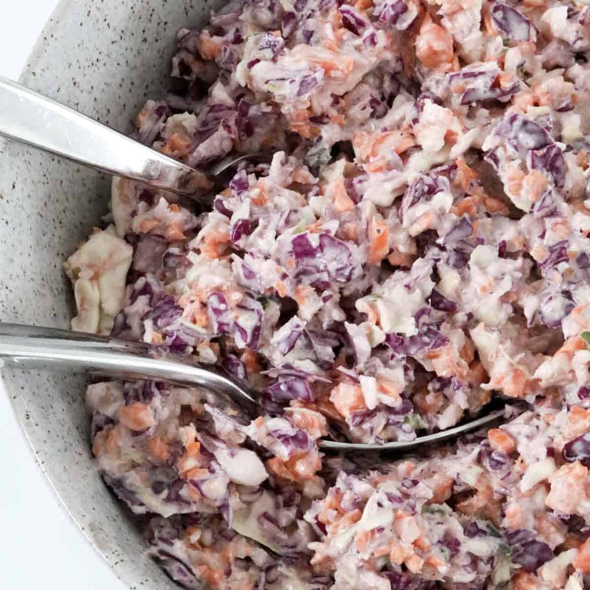 Salad servers in a bowl of creamy cabbage salad.