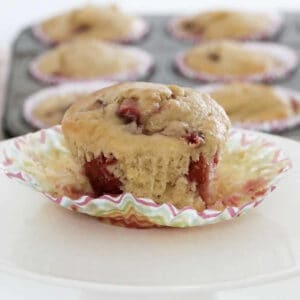 A banana muffin with chunks of strawberries on a paper case.