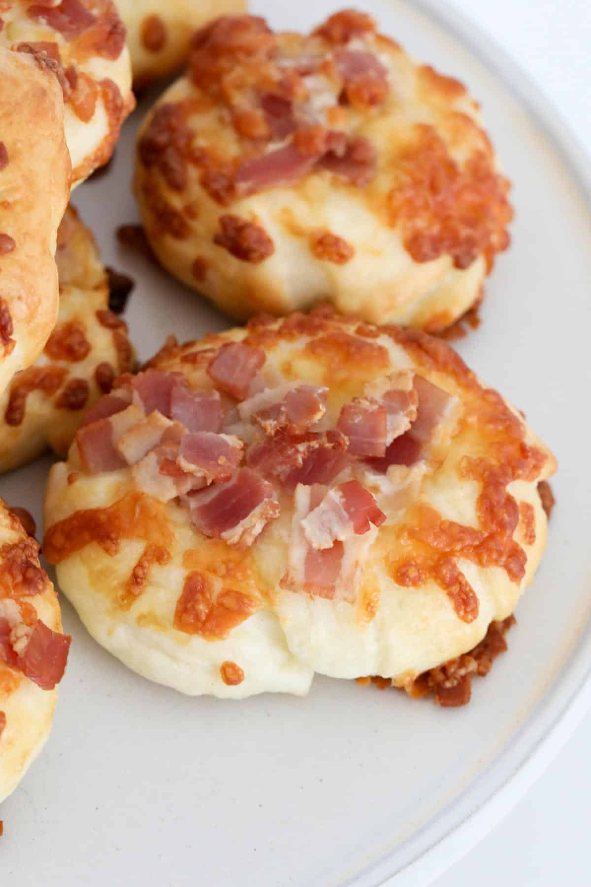 Bread rolls topped with golden cheese and bacon pieces.