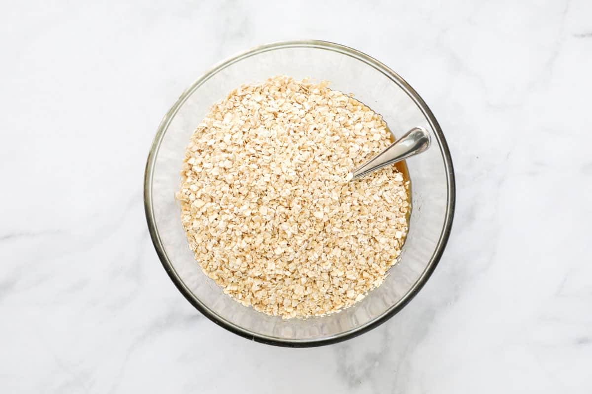 Quick oats added to mixture in a glass bowl with a metal spoon.