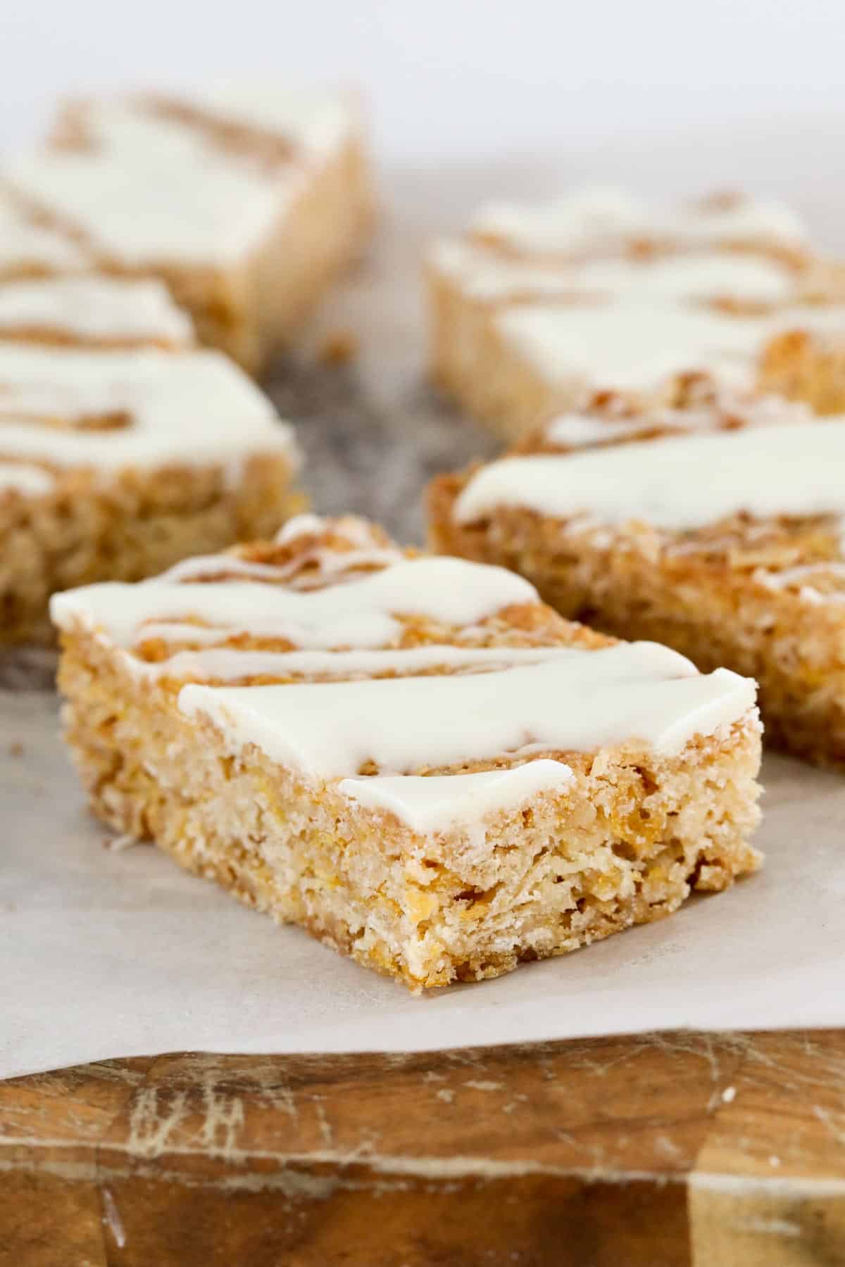 A piece of baked crunchy slice with white chocolate on top, placed on a wooden board.