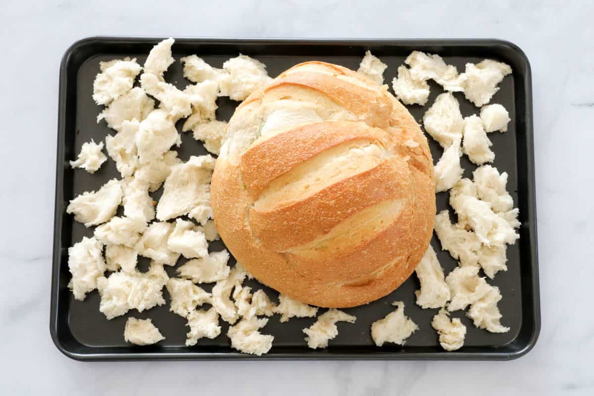 Cob loaf on a baking tray surrounded by torn pieces of bread.