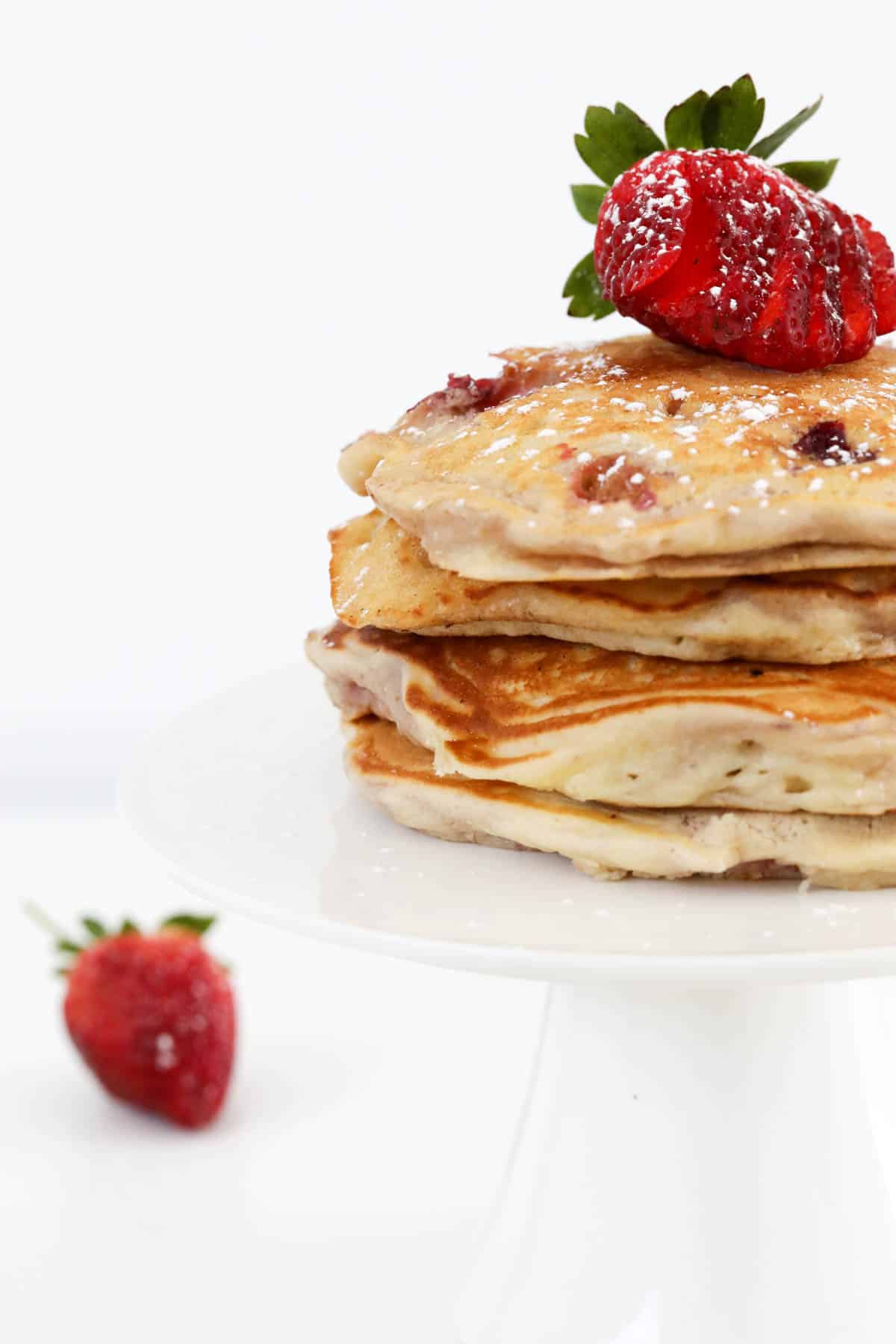Pancakes stacked on a cake stand with sliced strawberry on top.