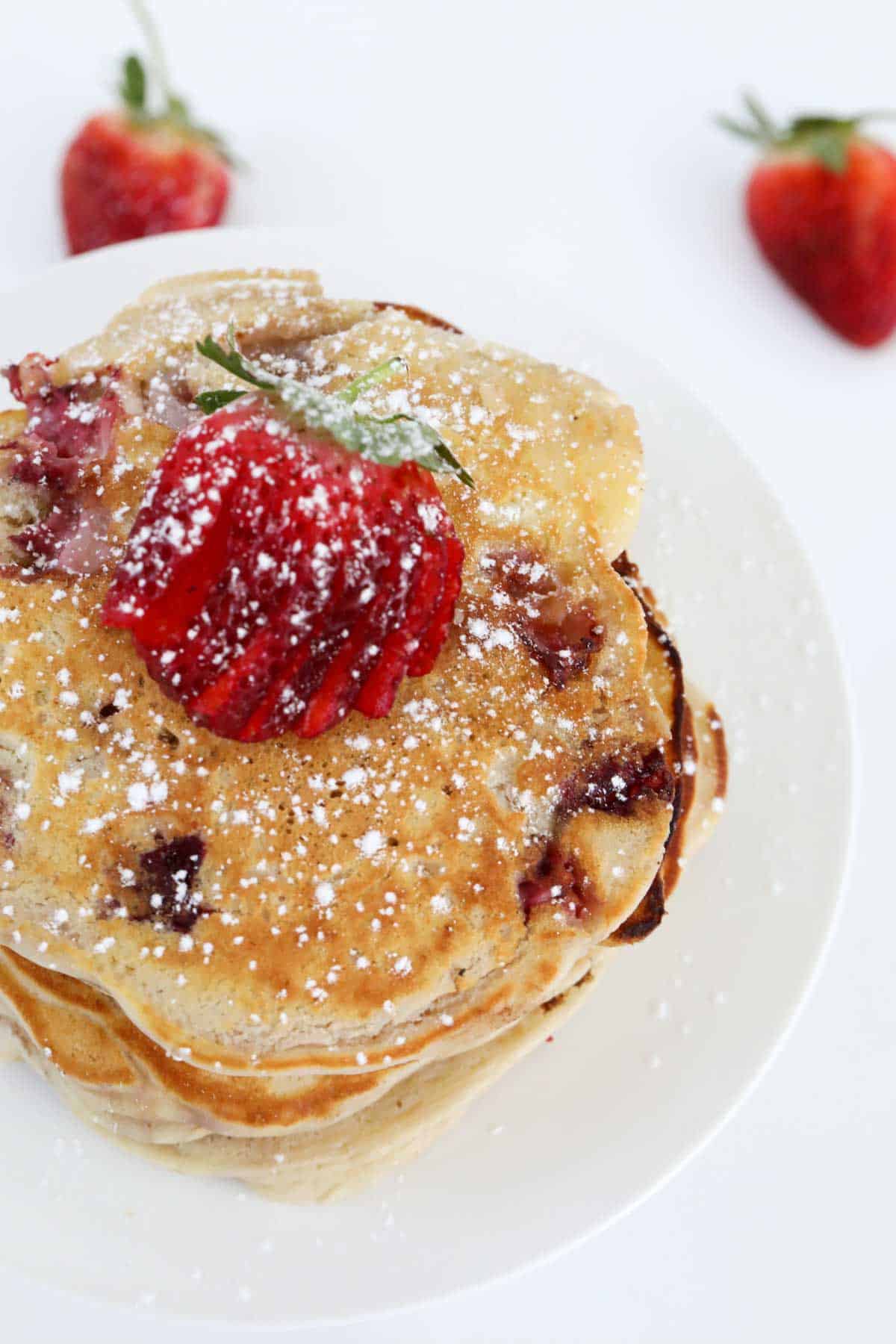 Looking down on a stack of pancakes with a sliced strawberry on top, dusted with icing sugar.