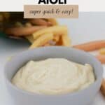 Creamy aioli in a small grey bowl with vegetable sticks in the background.