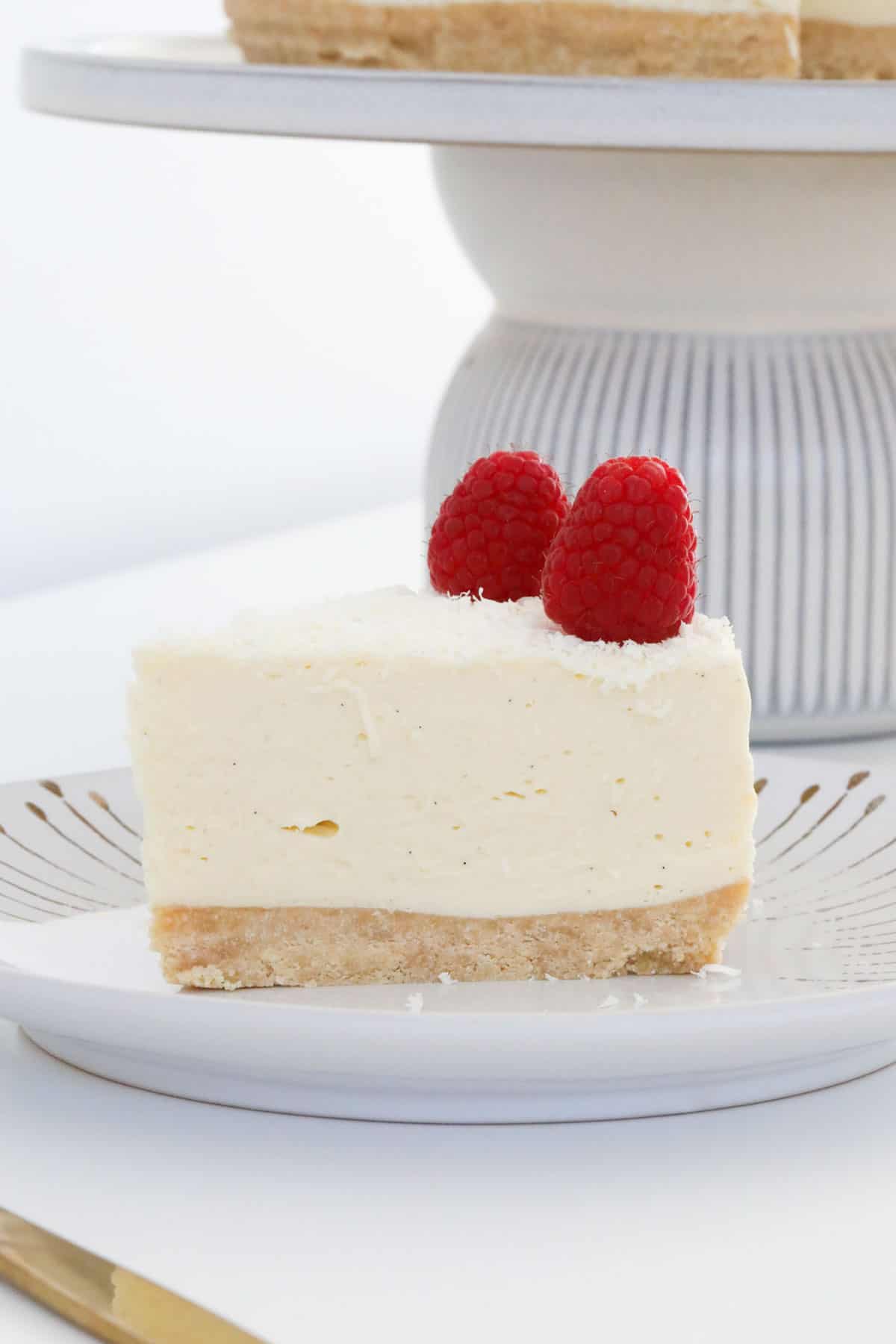A side view of a piece of cheesecake on a white plate, topped with fresh berries.