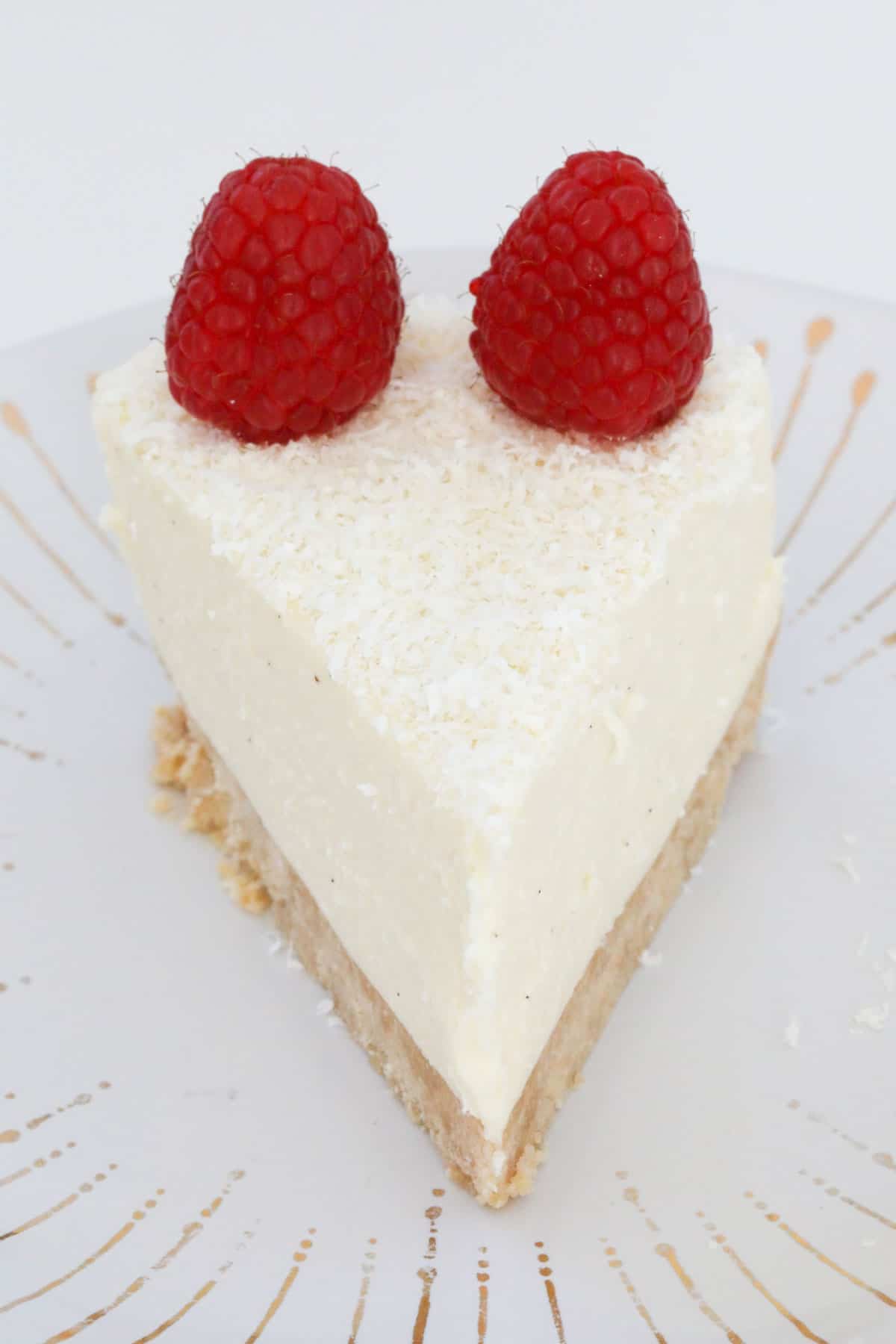 A slice of white chocolate cheesecake on a plate, topped with fresh raspberries.