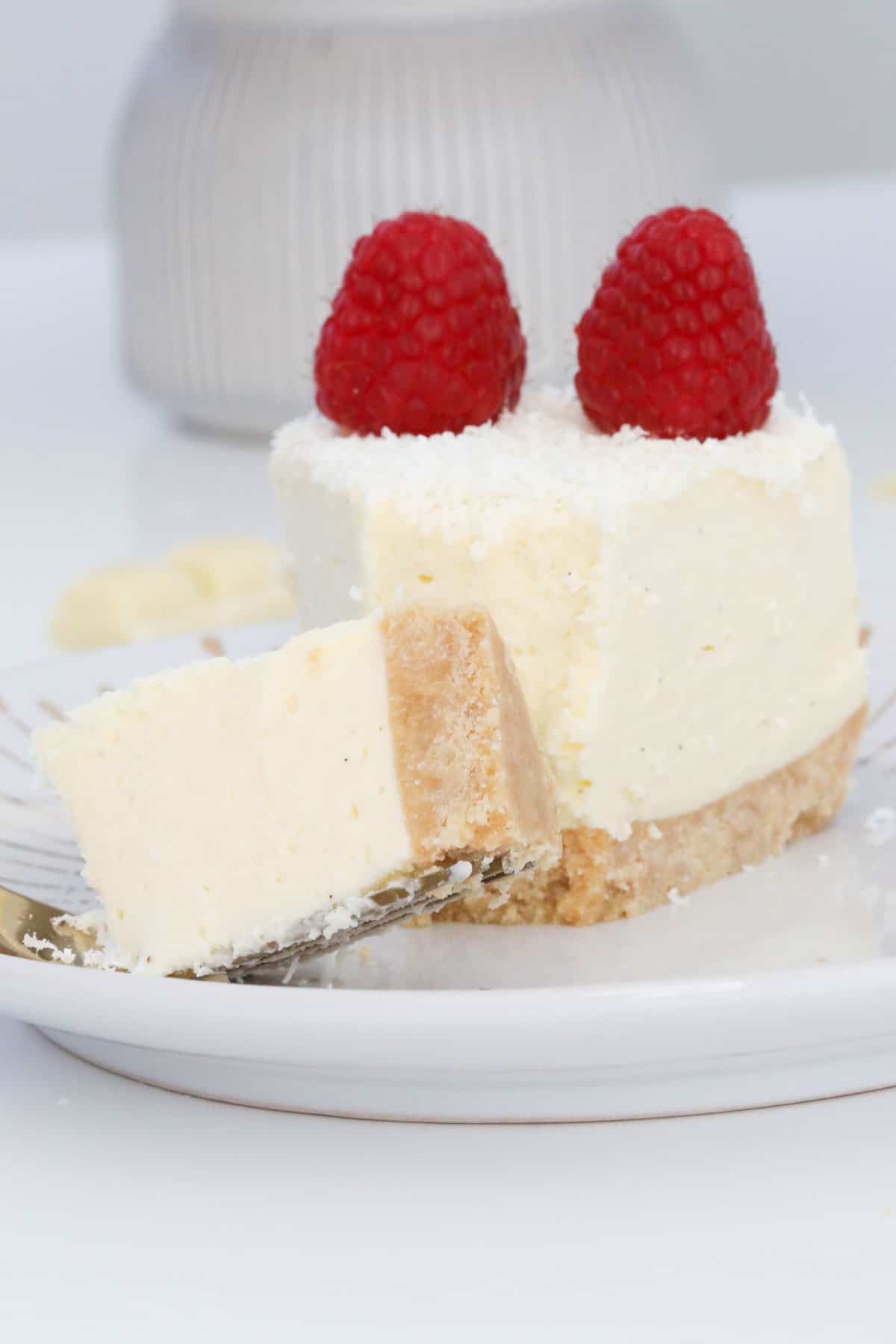 A piece of cheesecake on a plate with a bite-sized piece on a fork.
