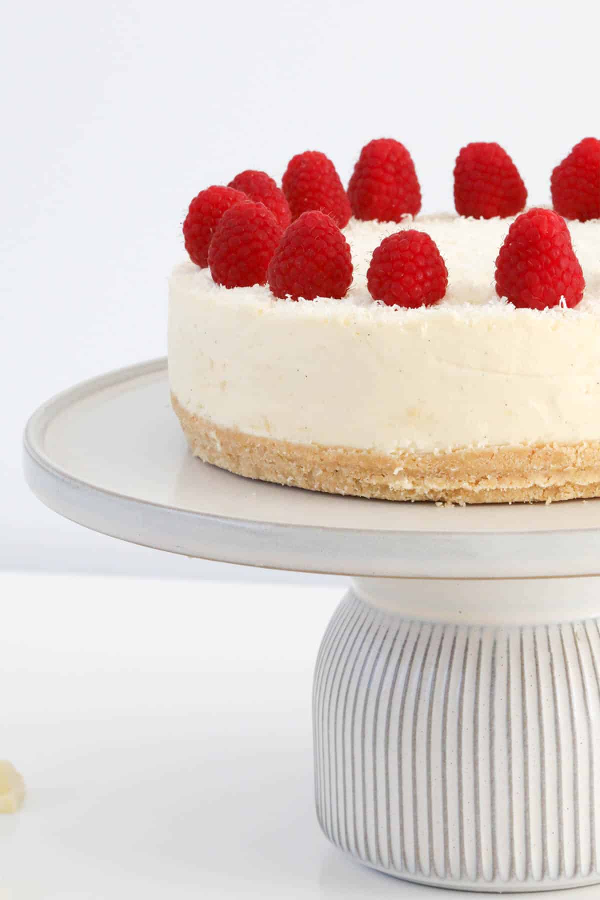 Cheesecake on a white stand, topped with raspberries.