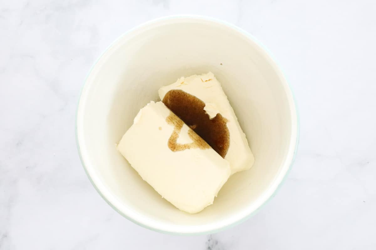Blocks of cream cheese and vanilla in a white bowl.