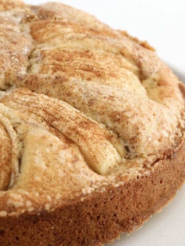 Apples and cinnamon on top of a round cake.