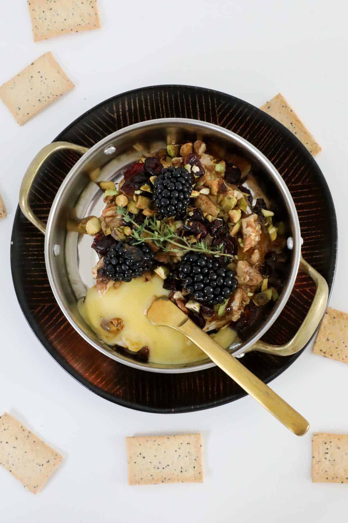 An overhead shot of a baked brie cheese with nuts, dried fruit anf fresh blackberries.