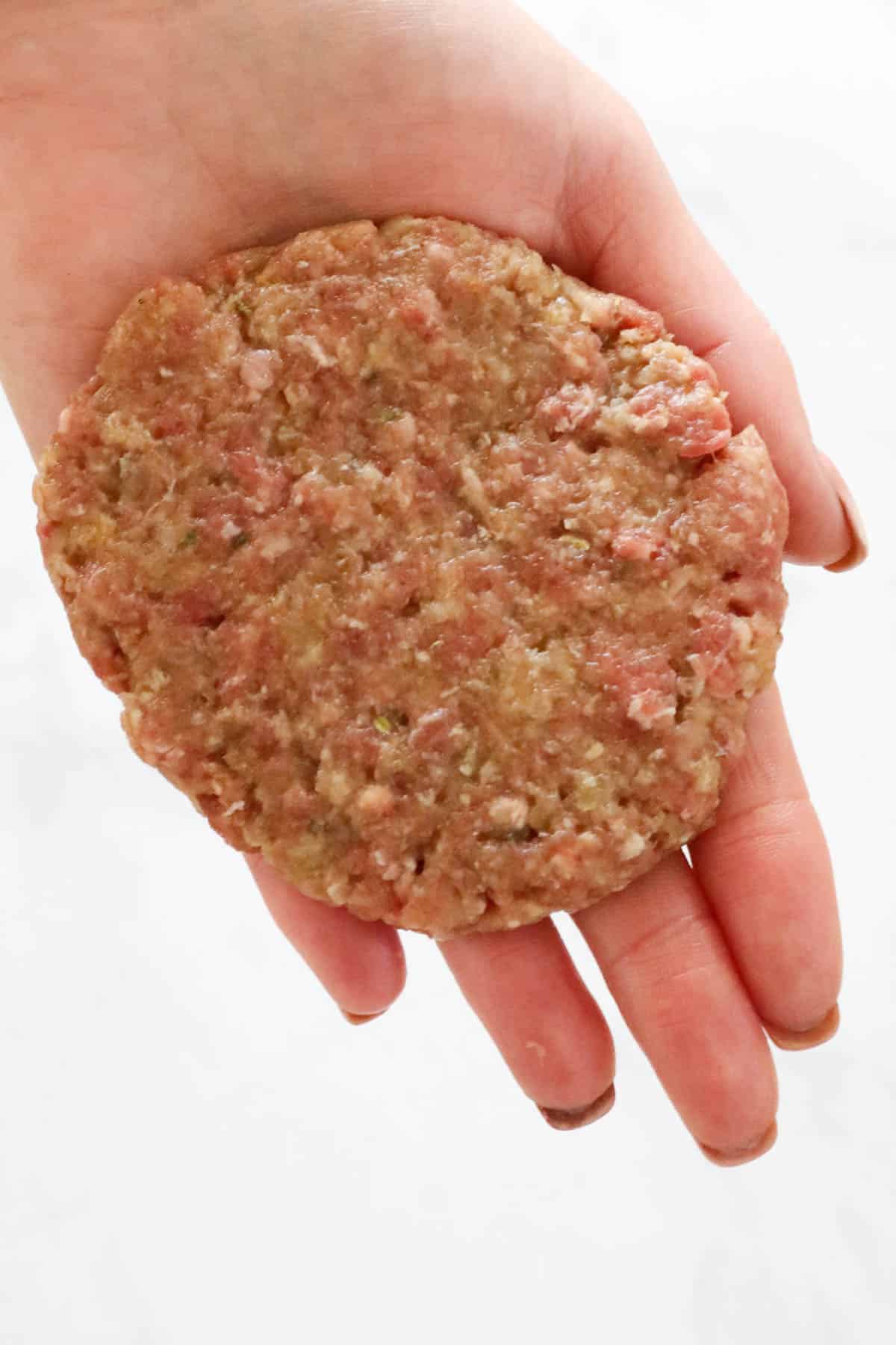 A hand holding a flat round meat patty.