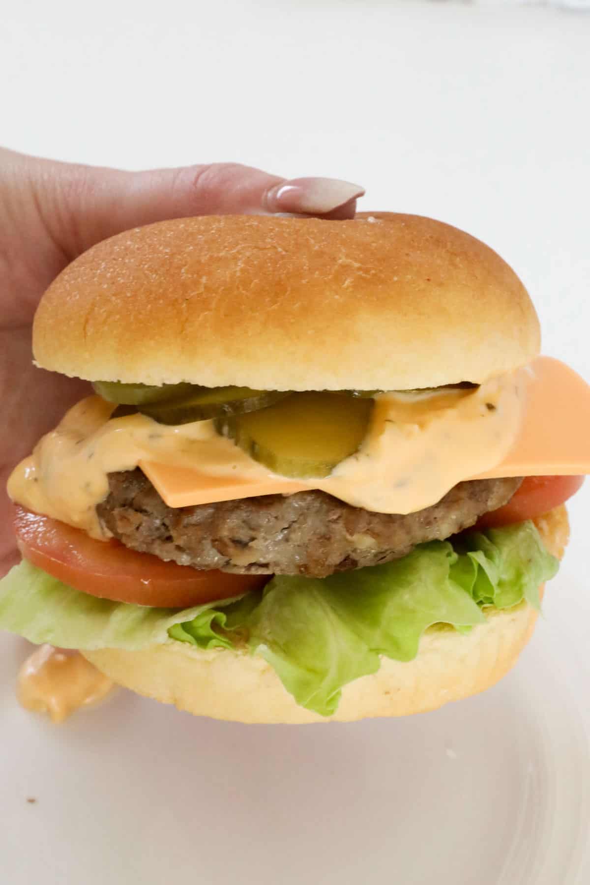 A hand holding a beef patty burger on a bun.