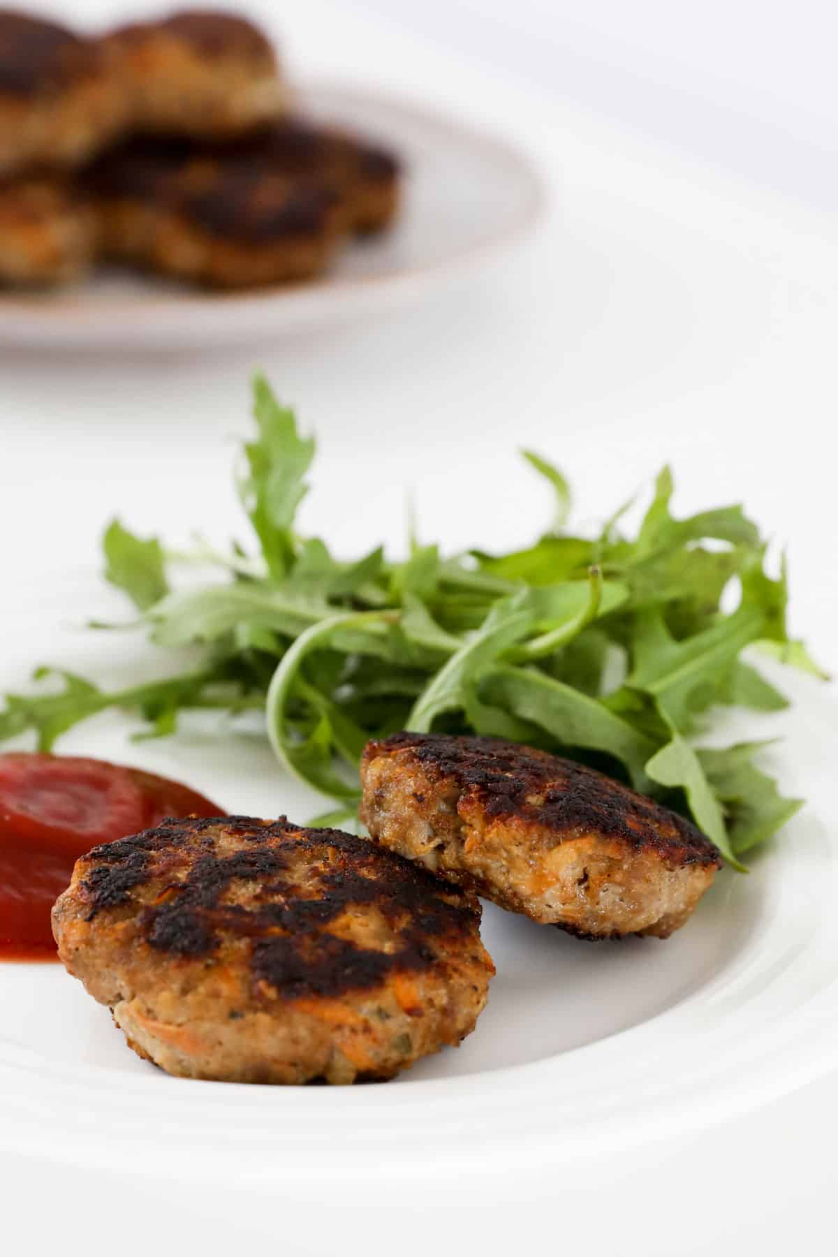 Golden beef rissoles on a plate with rocket and sauce.