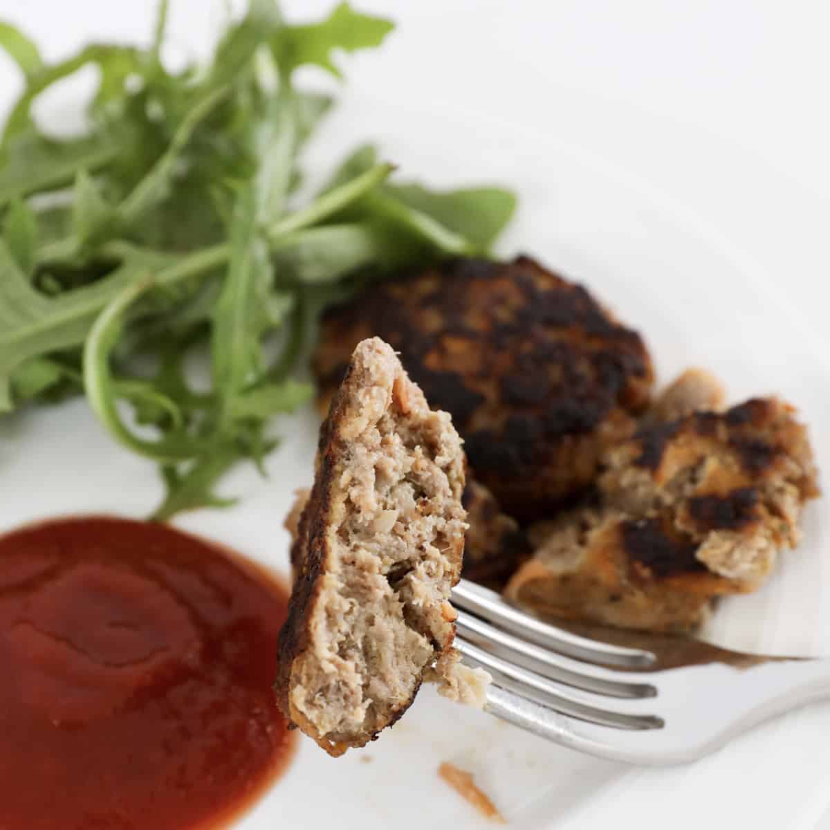 A beef rissole on a fork in front of rocket and sauce.