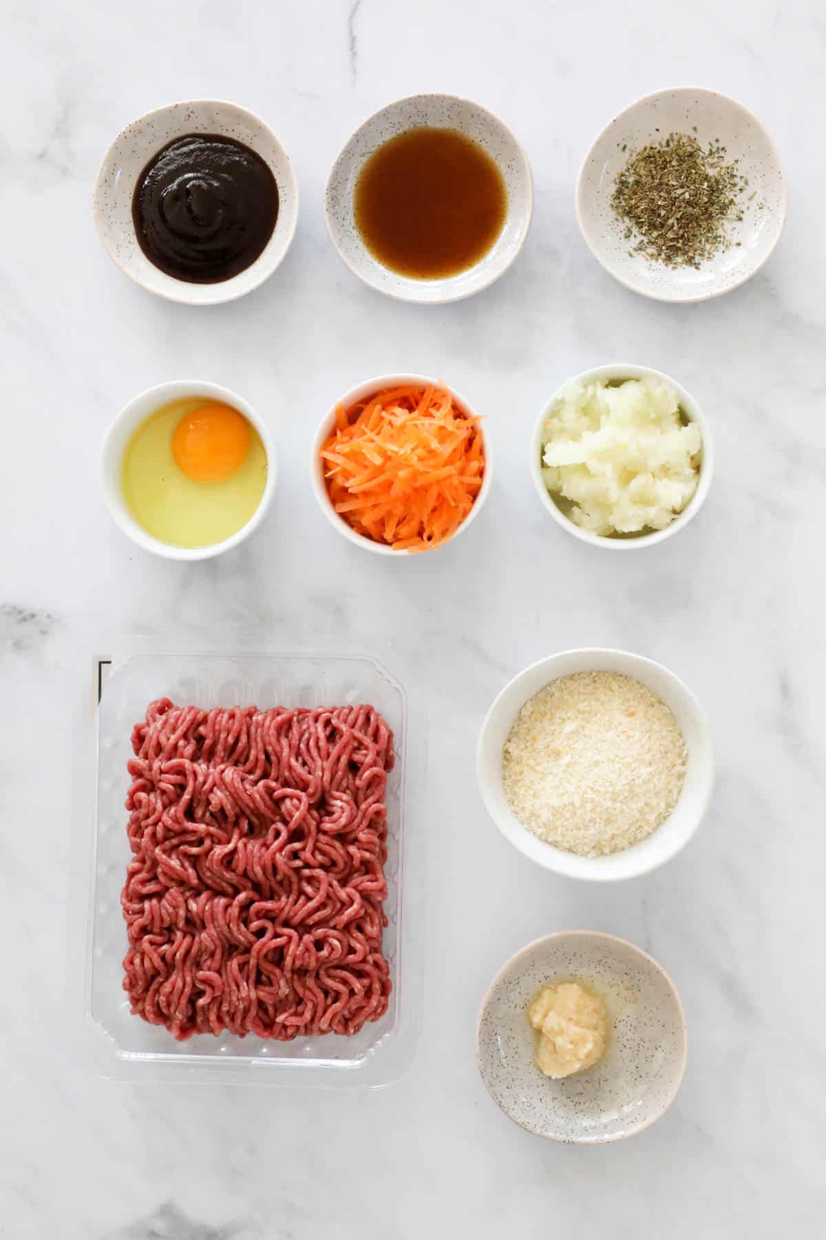The ingredients for meat patties in individual bowls on a bench top.