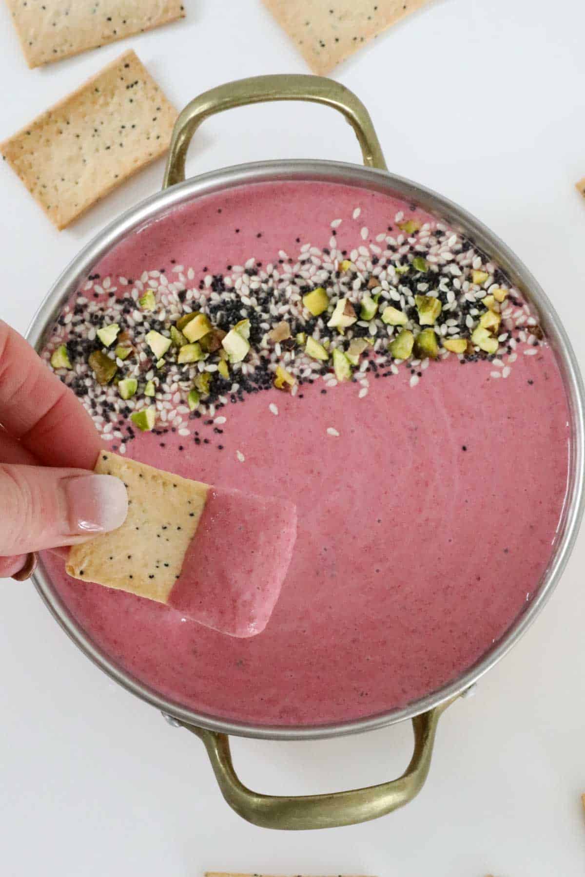 A cracker being dipped into a bowl of pink dip.