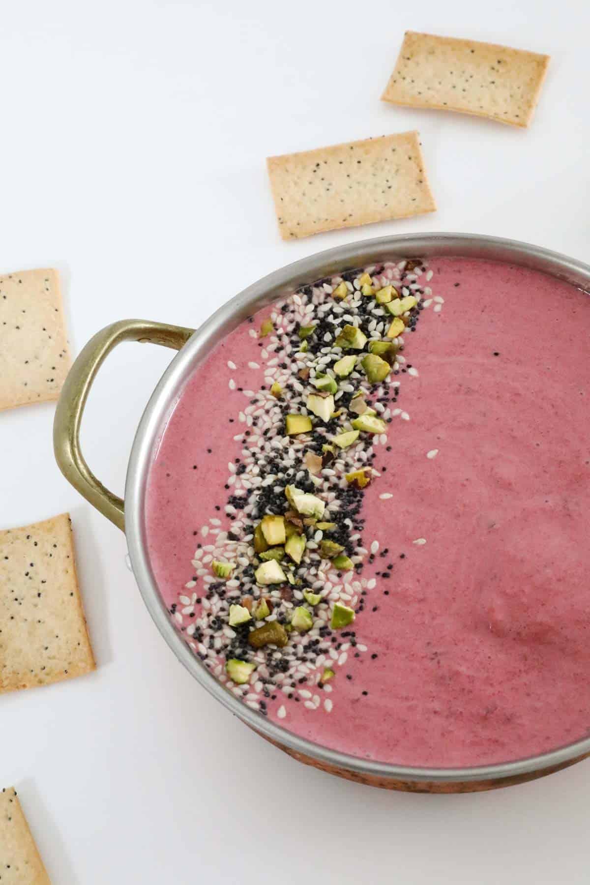 A bowl of colourful dip with lavosh crackers next to it.