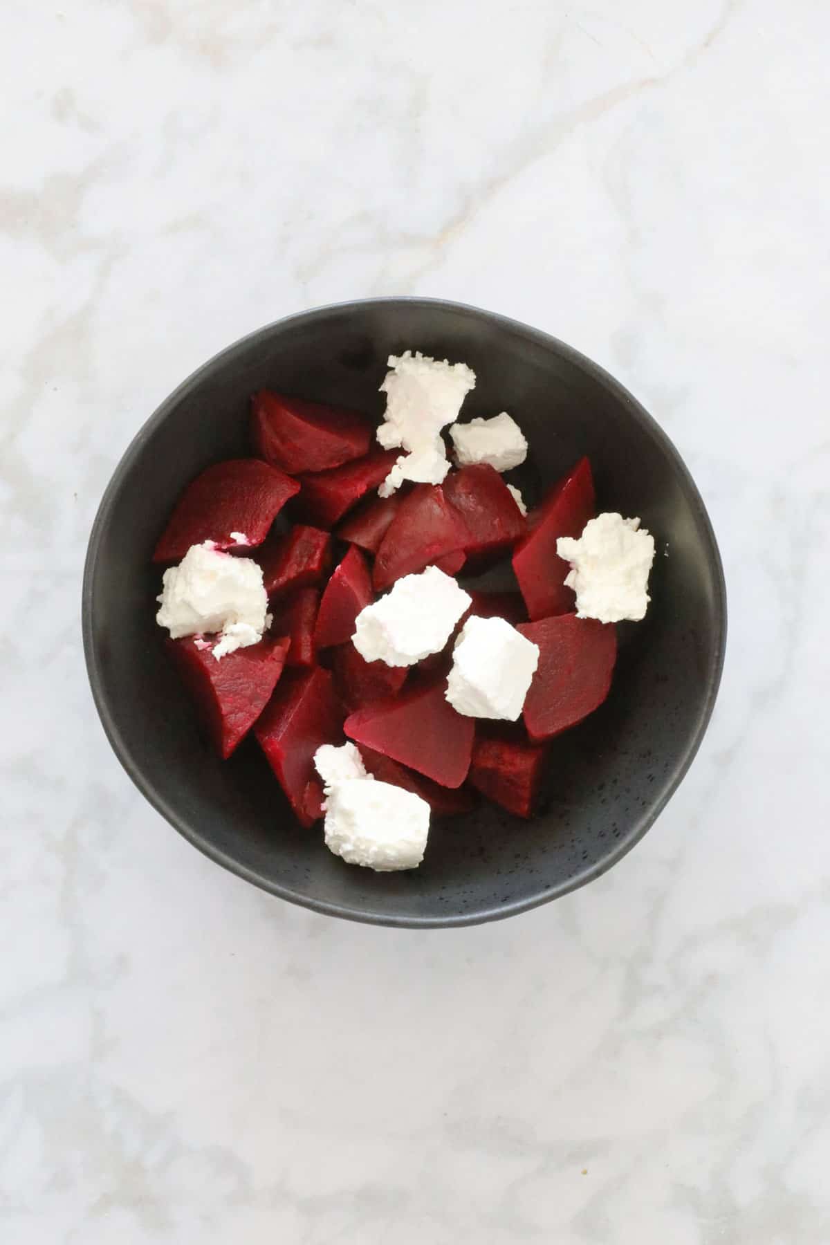 Chunks of beetroot and soft feta in a black bowl.