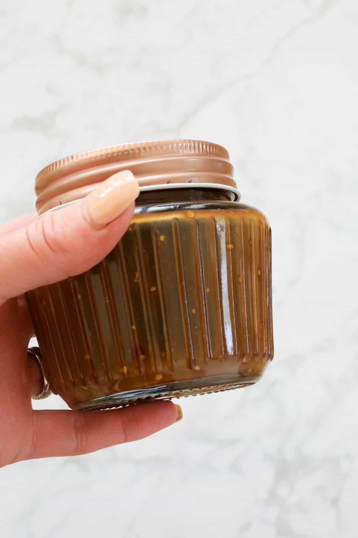 A hand holding a decorative jar filled with an honey, mustard and balsamic dressing.