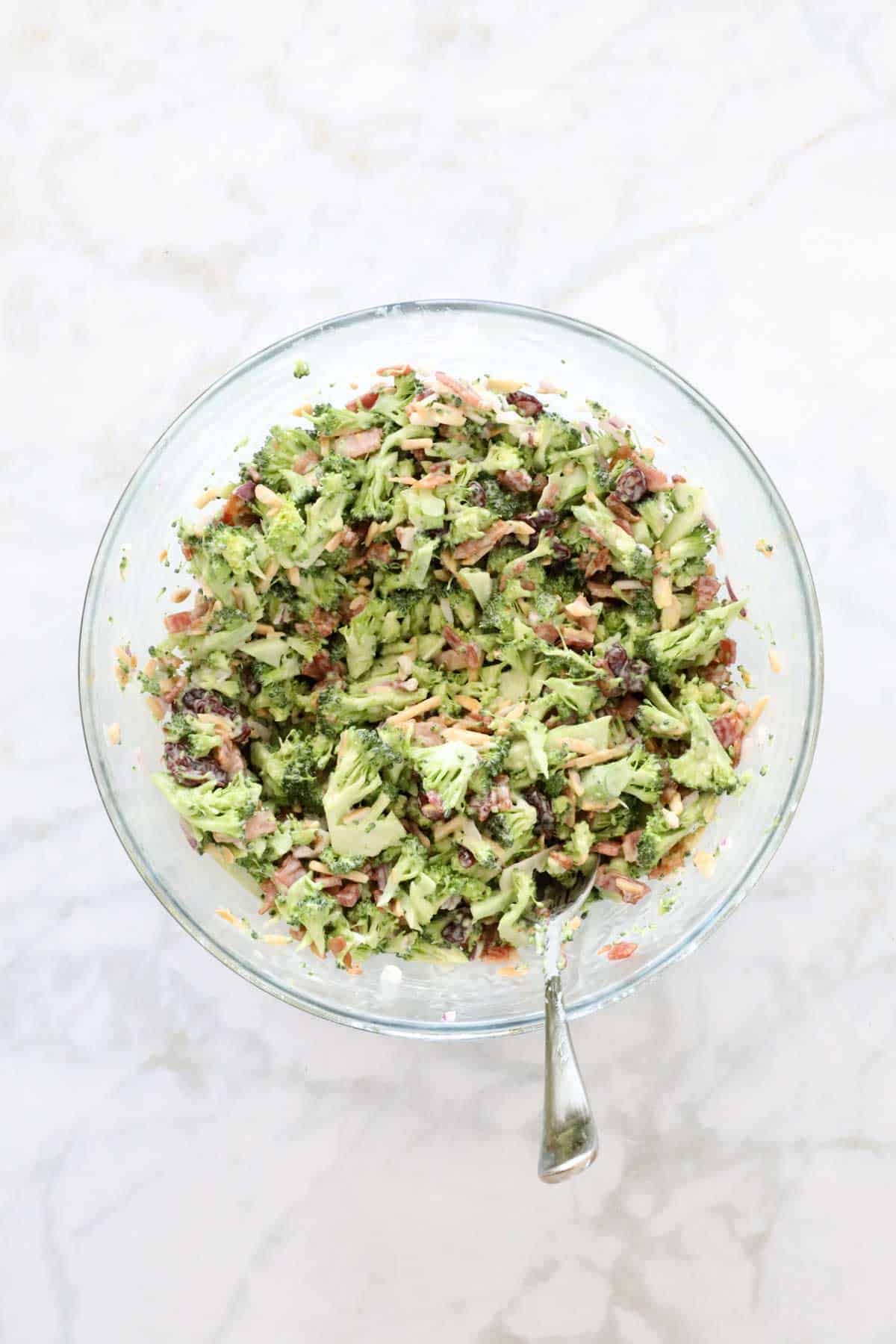 Creamy broccoli salad with bacon mixed together in a glass bowl.