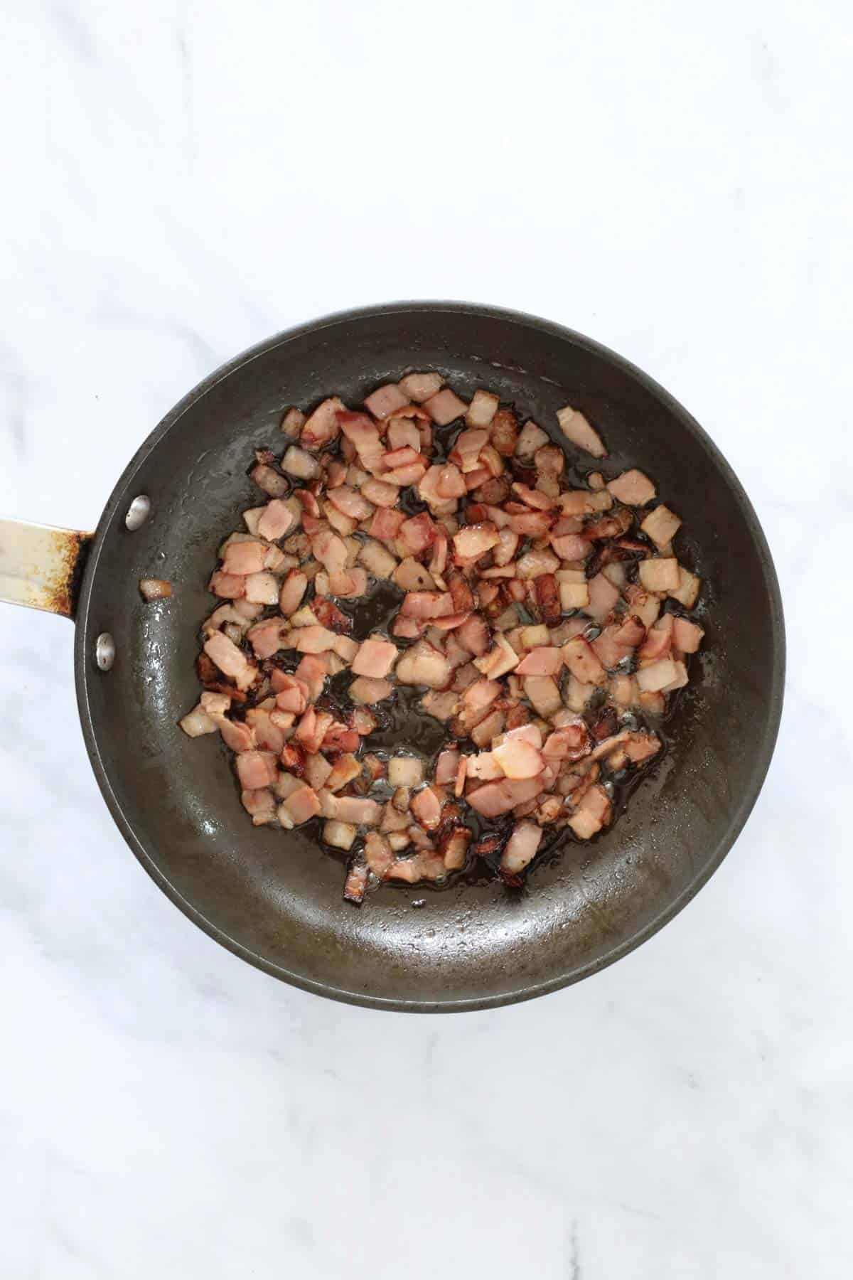 Diced crispy bacon in a frying pan.