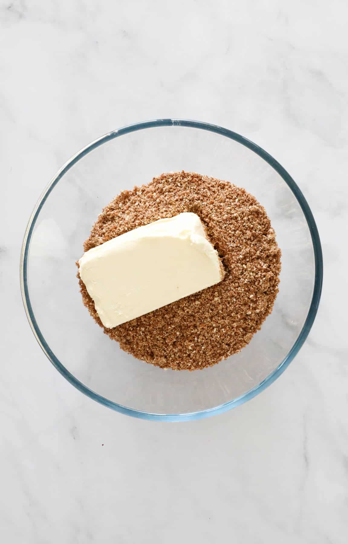 A block of cream cheese placed in a bowl of crushed Tim Tam biscuits.