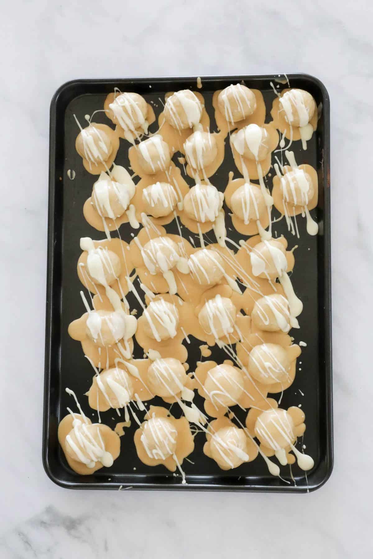 Cheesecake balls rolled in melted caramel chocolate and then drizzled with white chocolate, served on a tray.