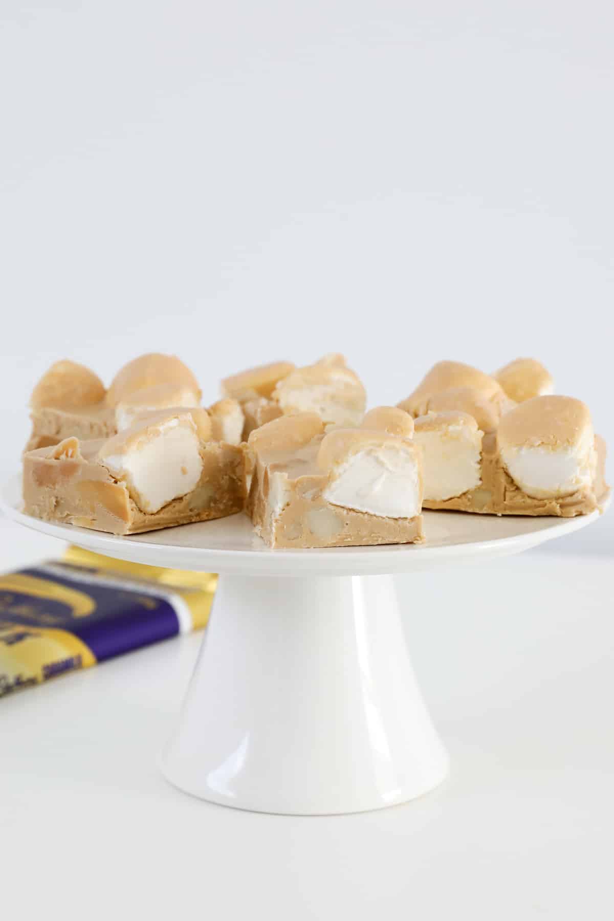 Pieces of caramel and white marshmallow rocky road on a white cake stand.