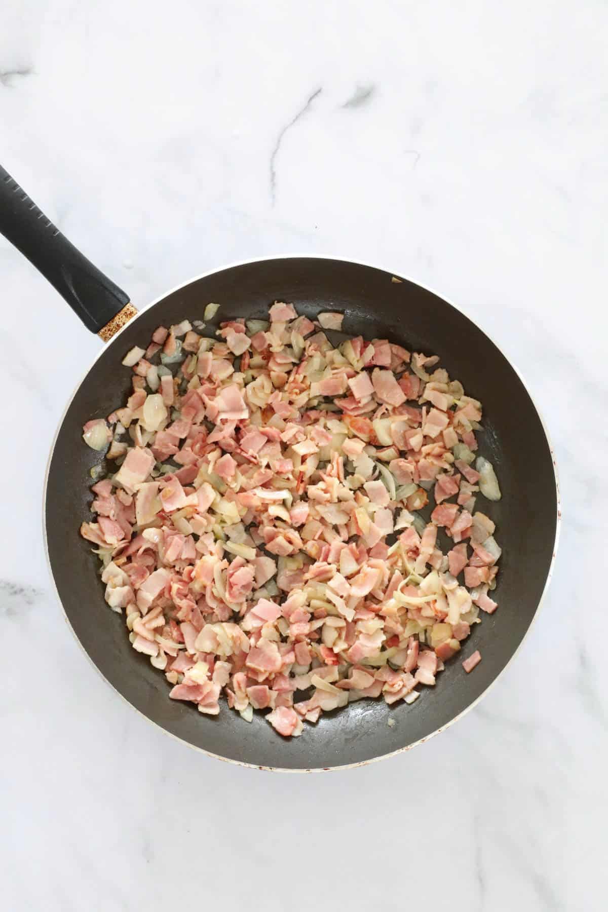 Chopped bacon and onion sauring in a frying pan.