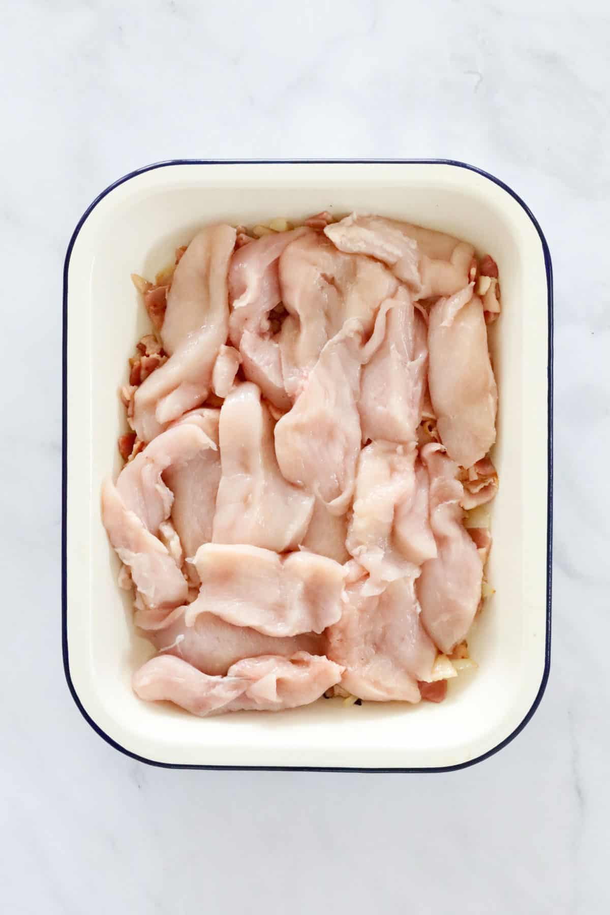 Cut raw chicken breasts on top of bacon and onions in a casserole dish.