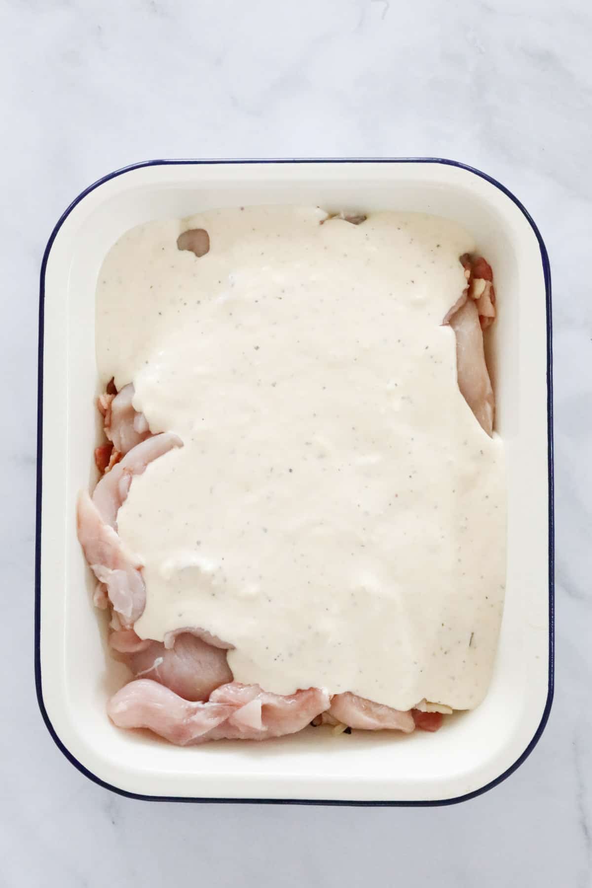 Creamy ranch sour cream sauce poured over chicken pieces in a baking dish.
