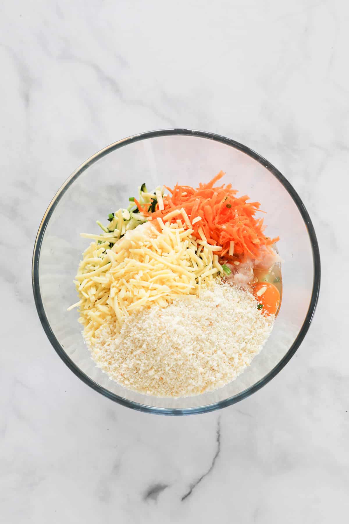 Breadcrumbs, grated veggies and cheese in a glass bowl.